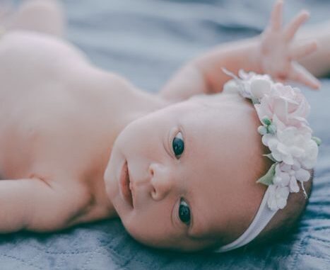 A cute newborn baby wearing a floral headband, lying on a soft blanket.