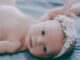 A cute newborn baby wearing a floral headband, lying on a soft blanket.